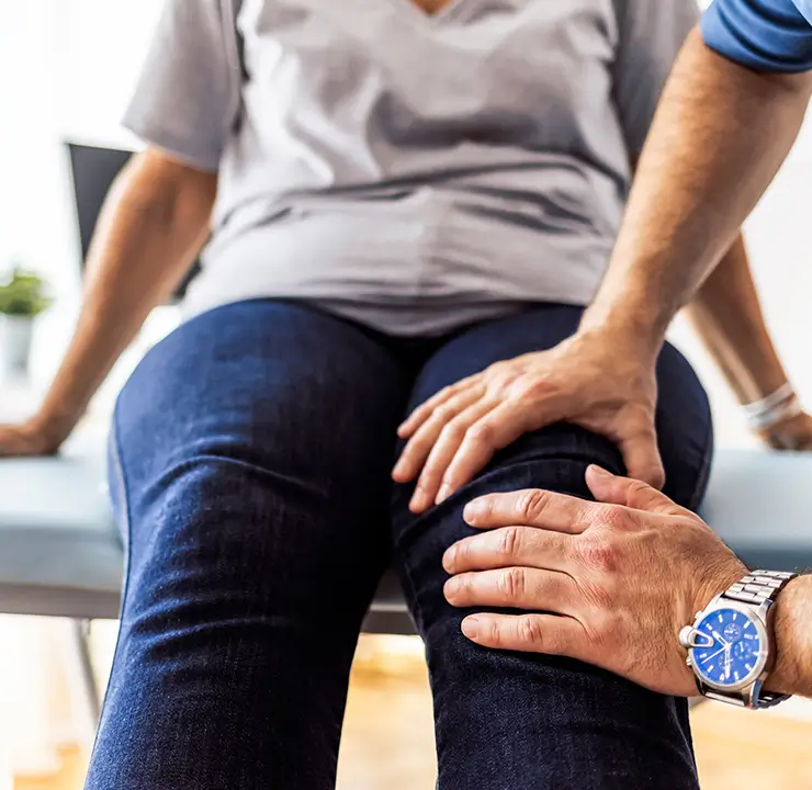 A person receiving a knee examination from someone wearing a blue watch.