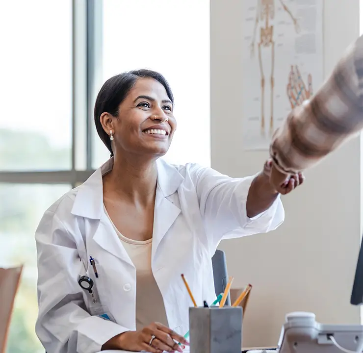 A smiling doctor in a white coat shakes hands with a patient in a bright office.