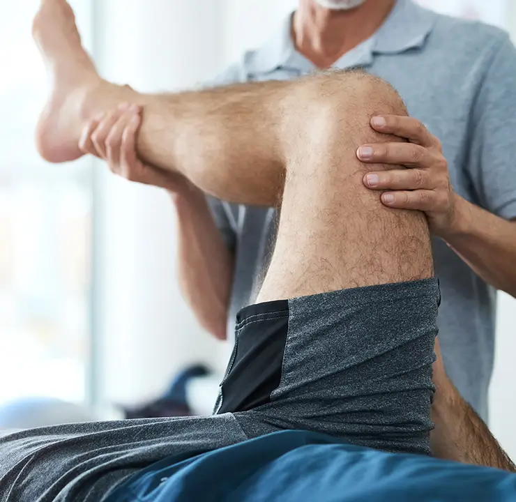 A physical therapist assists a person in stretching their leg, focusing on the knee in a bright, clinical setting.