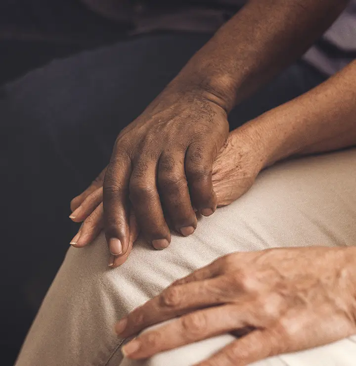 Two people are sitting close together, gently holding hands, conveying a sense of support and comfort.