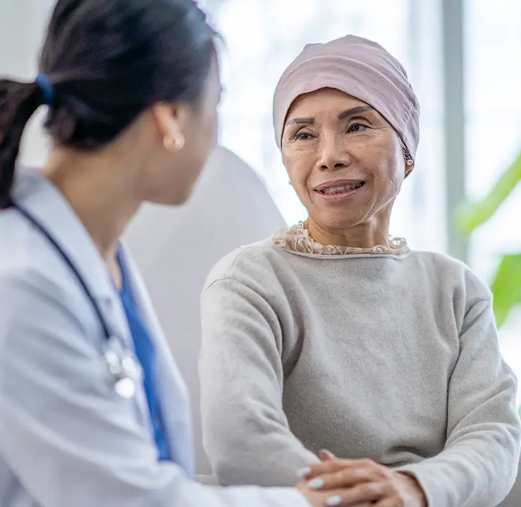 A doctor and a patient wearing a headscarf are sitting and talking in a well-lit room.