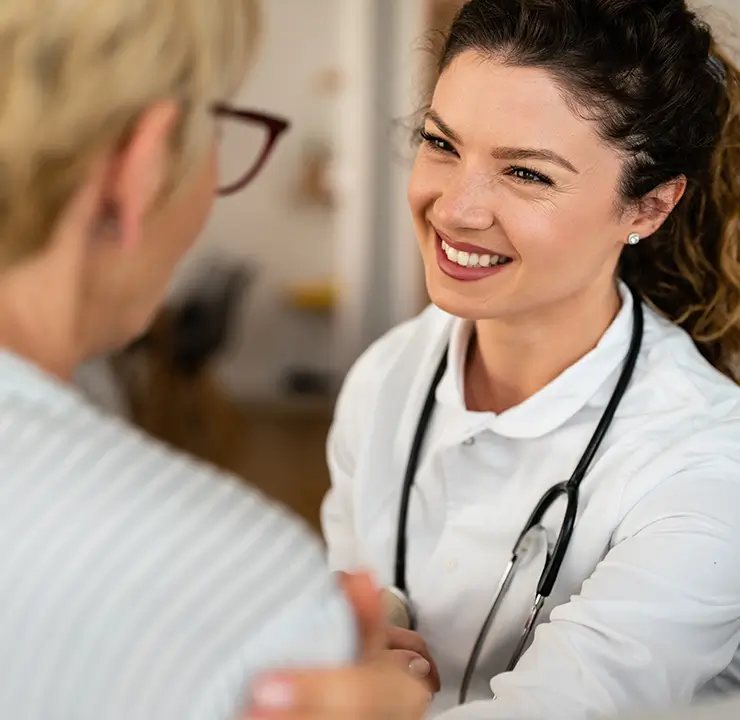 A smiling healthcare professional with a stethoscope talks to a patient, who is facing away from the camera.