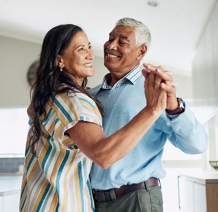 An older couple smiling while dancing together in a kitchen.