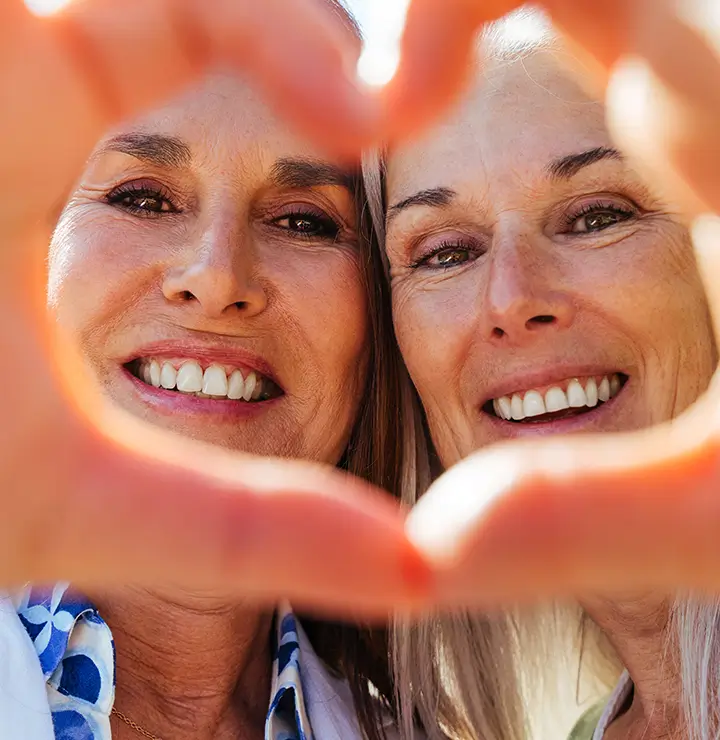 Two smiling people framed by hands forming a heart shape.