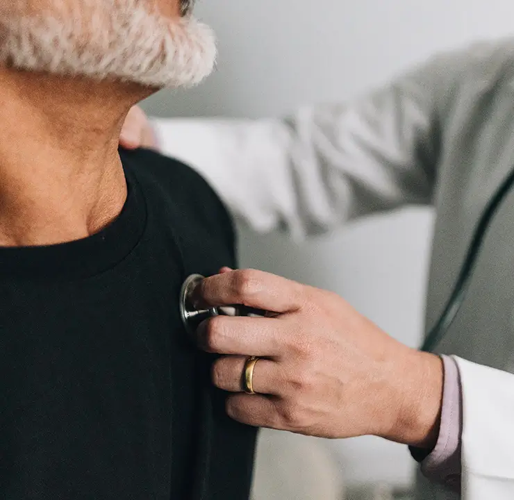 A doctor in a white coat uses a stethoscope to listen to a patient's chest.