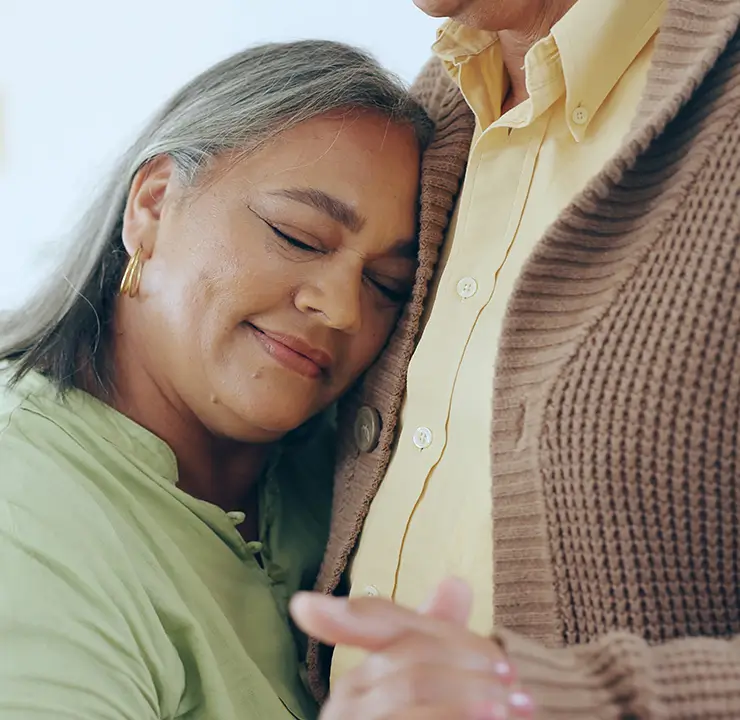 A woman in a green shirt rests her head on a person's chest, eyes closed, appearing content and peaceful.