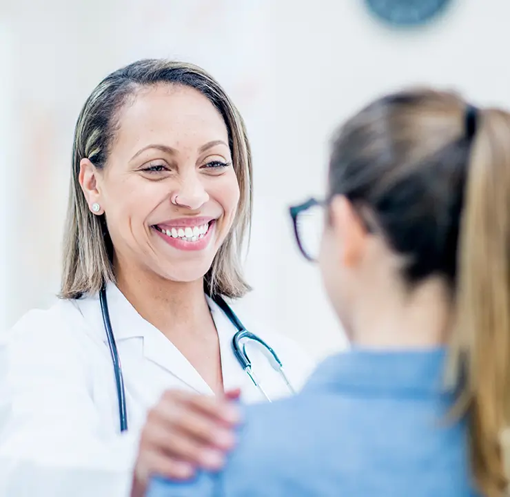 A doctor with a stethoscope smiles and interacts warmly with a patient in a medical setting.