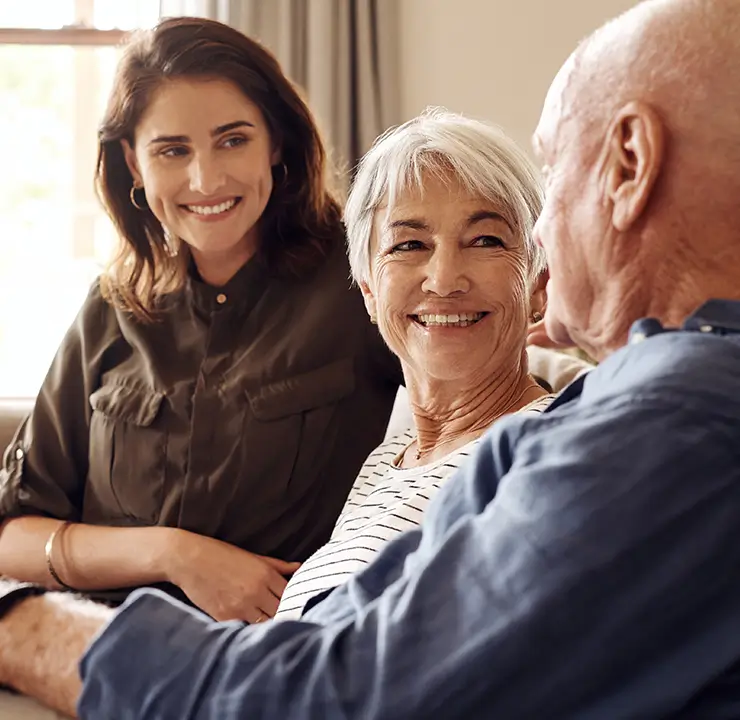 Three people sitting together on a couch in a cozy living room, engaging in a cheerful conversation.