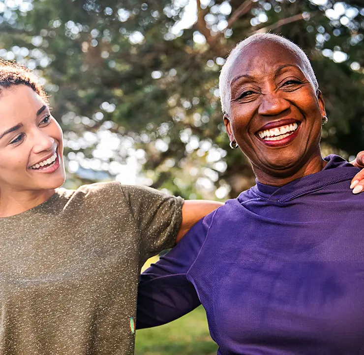 Two people smiling and embracing outdoors, with trees in the background.