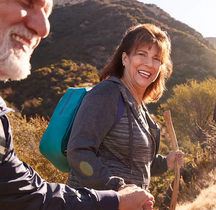 A group of people smiling while hiking in a mountainous area with trees and sunshine.