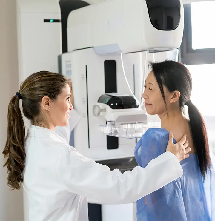 a female patient having her breast examined by a machine while speaking to doctor