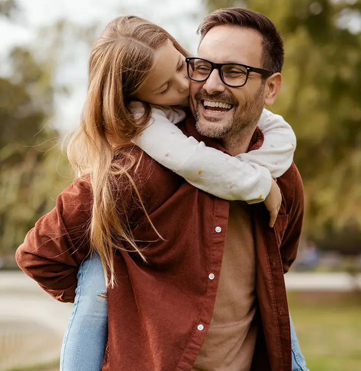 a father laughs while giving his daughter a piggy back ride