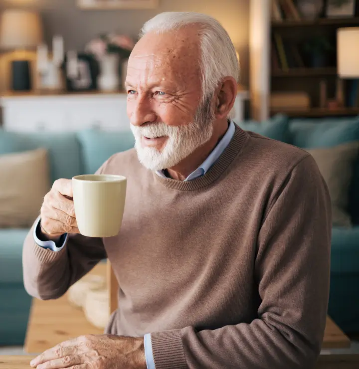 elderly man enjoys a cup of coffee while looking out a window
