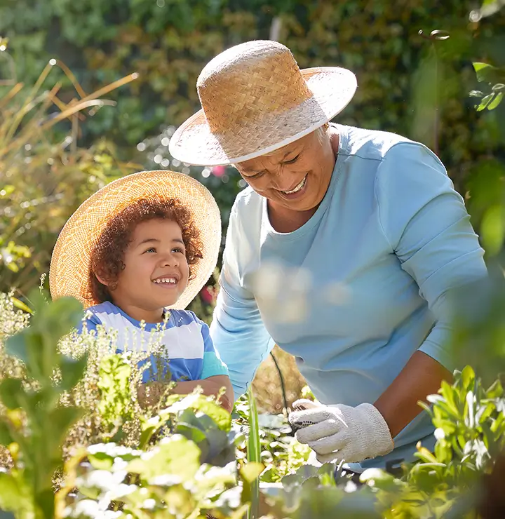 an elderly women joyfully shows her grandson how to garden on a bright sunny day