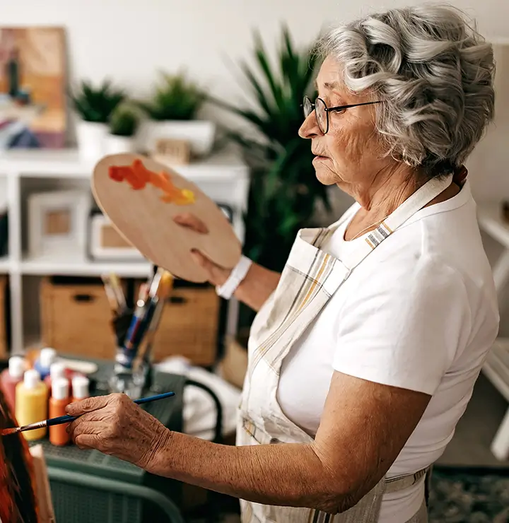 Elderly women with glasses leisurely paints with her palette in hand