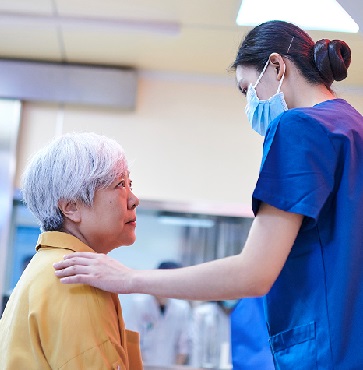 Senior Asian woman looking concerned, speaks with doctor in blue scrubs in front of MRI machine