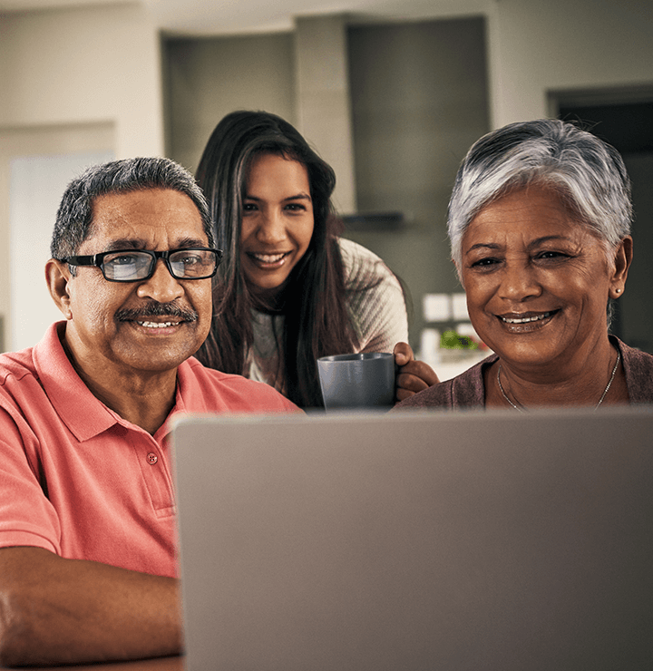 an elderly couple and their daughter look at a computer screen together