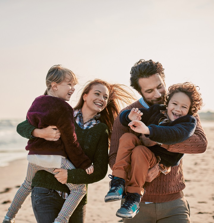 A family strolls along the beach holding their children in the fall sunshine