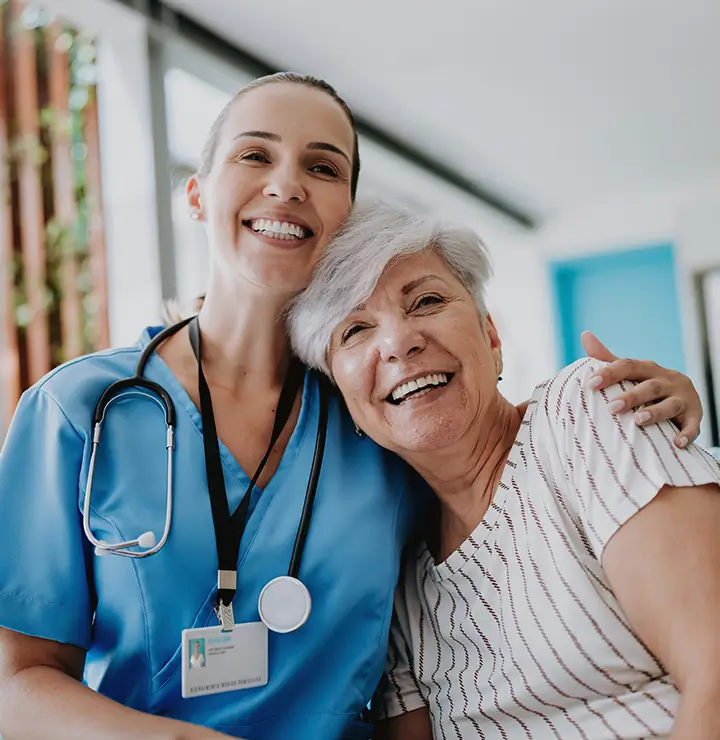 A nurse hugging a elderly patient with a smile on their face.
