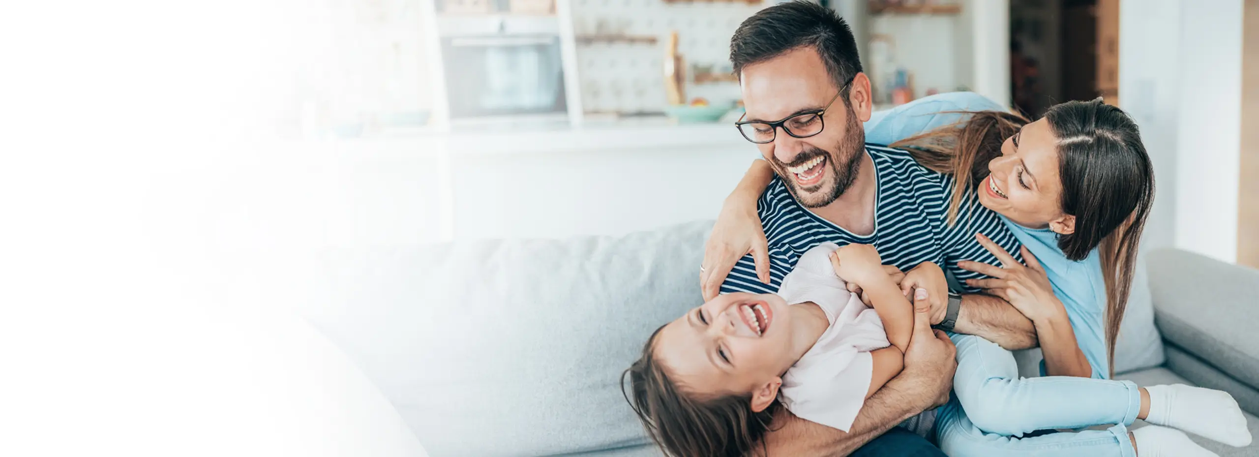 Parents playing with their young child on a couch at home.