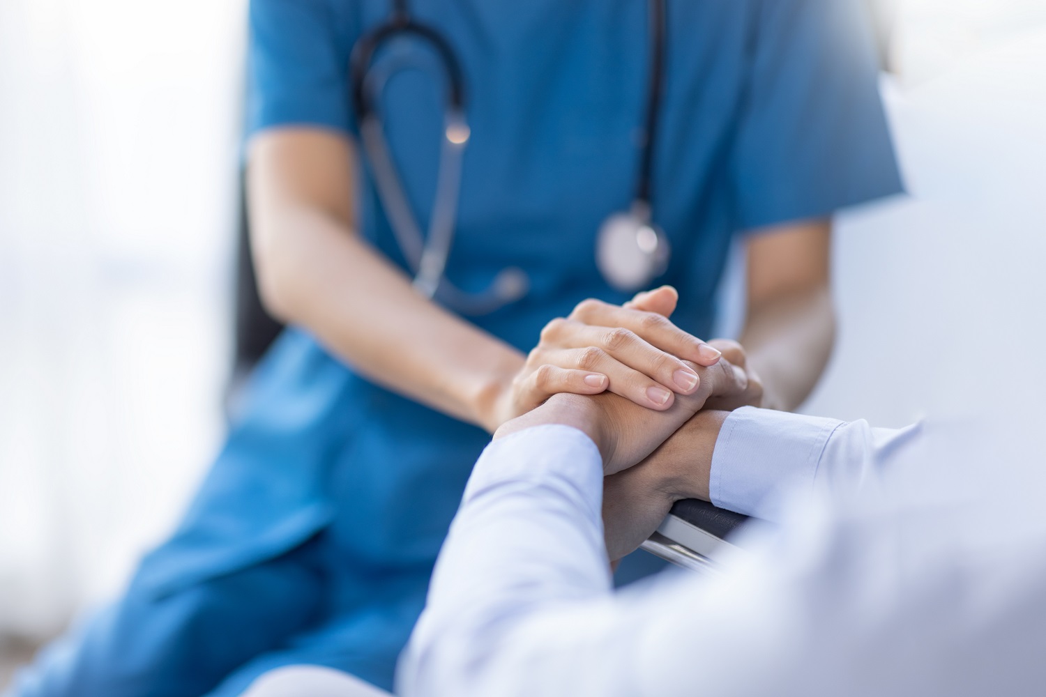 A healthcare professional in blue scrubs holds a patient's hand